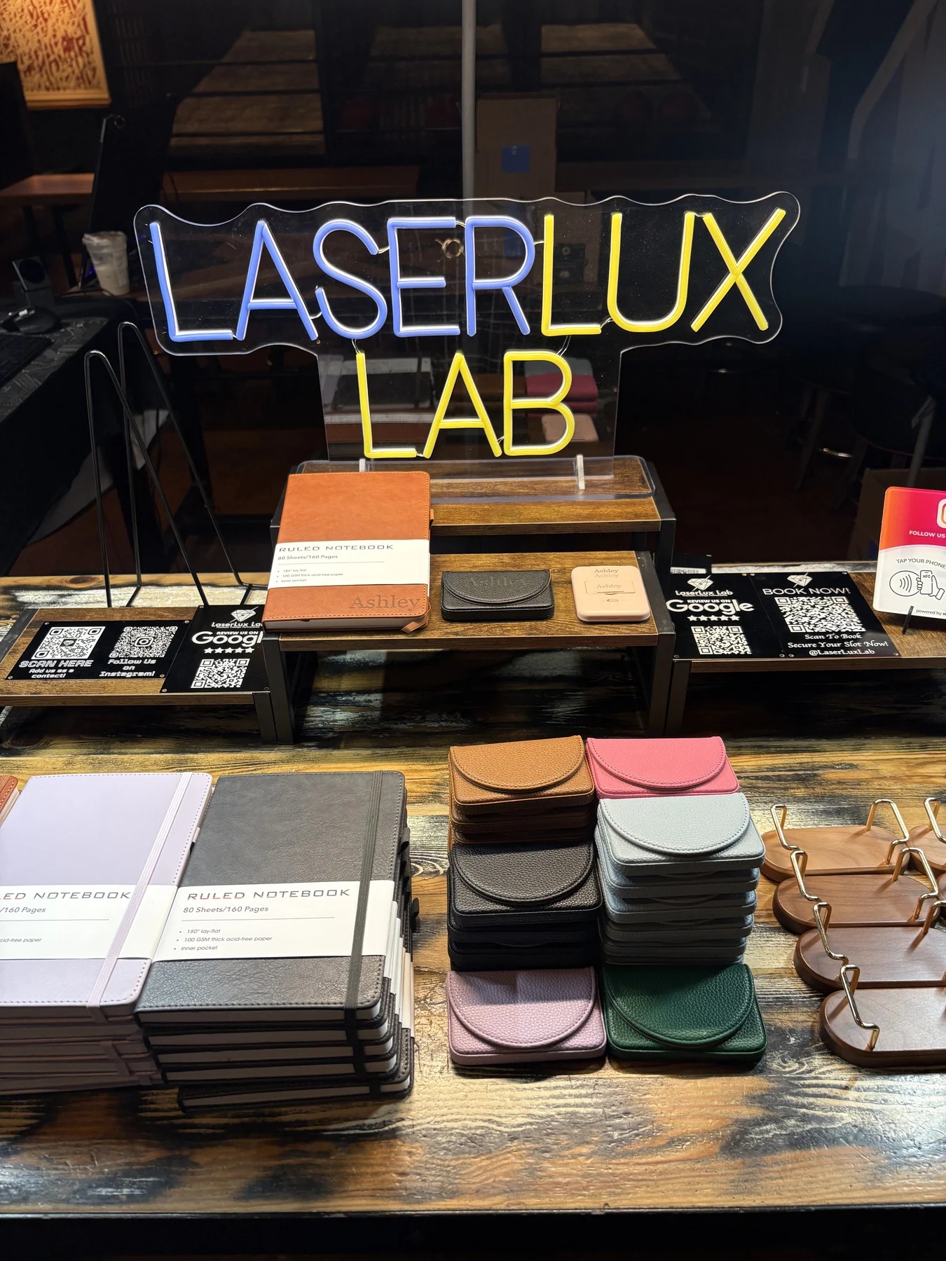 LaserLux Lab neon sign above a display of notebooks, leather cases and engraved items